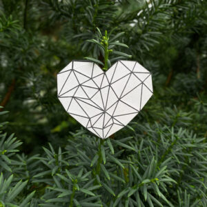 Heart-shaped reflector badge with intricate geometric pattern hanging against lush green tree background