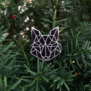 Black fox shaped reflector badge with geometric pattern, displayed against a vibrant green tree background