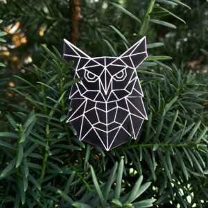 Black owl shaped reflective badge with geometric pattern on a green background