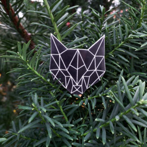 Black cat head shaped reflector badge with geometric pattern, displayed against a vibrant green tree background